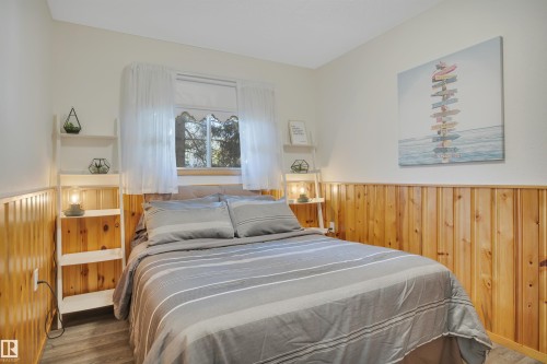 Bedroom featuring natural wood paneling, wood-finish flooring, a window with a wood-frame, and light-toned walls - 305 3 St, Rural Wetaskiwin County, AB - Indoor Photo Showing Bedroom