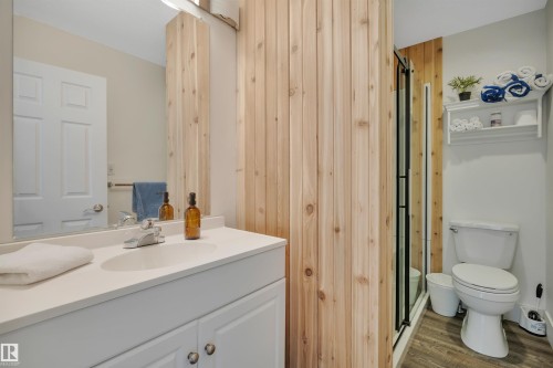 Bathroom featuring a white vanity with integrated sink, a wall-mounted mirror, wood-finish flooring, a glass-enclosed shower, and a toilet - 305 3 St, Rural Wetaskiwin County, AB - Indoor Photo Showing Bathroom