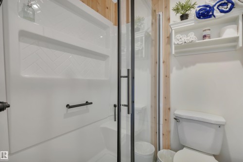Modern bathroom featuring a white shower enclosure with herringbone-patterned tile detailing, a clear glass shower door with matte black hardware, and a white toilet - 305 3 St, Rural Wetaskiwin County, AB - Indoor Photo Showing Bathroom