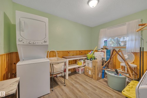Dedicated laundry area featuring a stacked washer and dryer, wood-finish flooring, and a wood panel wainscoting - 305 3 St, Rural Wetaskiwin County, AB - Indoor Photo Showing Laundry Room