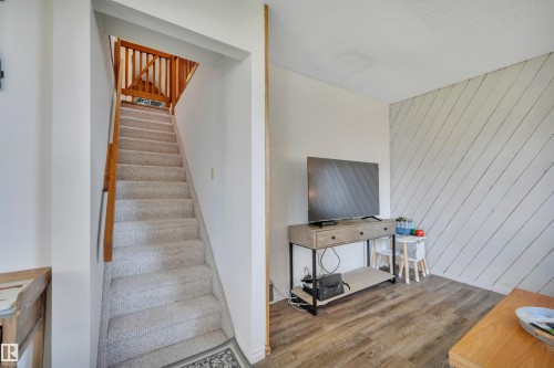 Carpeted staircase with wooden handrails, featuring white walls and a visible wood-finish flooring in the foreground - 305 3 St, Rural Wetaskiwin County, AB - Indoor Photo Showing Other Room