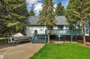 Stucco exterior residence featuring a dark shingle roof, an elevated wooden deck with railings, and mature evergreen trees providing natural screening - 305 3 St, Rural Wetaskiwin County, AB  - Outdoor With Deck Patio Veranda 