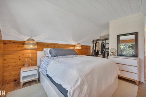 Bedroom featuring sloped white planked ceilings, wood-paneled walls, built-in shelving, white dresser with mirror, and a window - 305 3 St, Rural Wetaskiwin County, AB - Indoor Photo Showing Bedroom