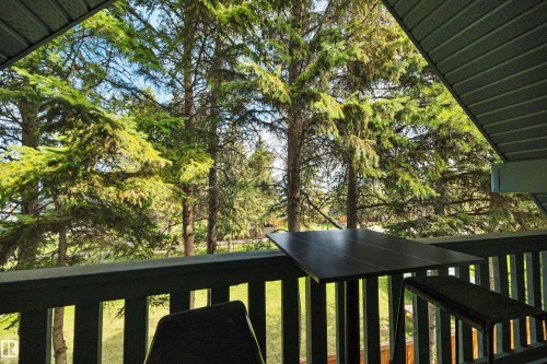 Covered outdoor balcony featuring a slatted railing and a backdrop of mature evergreen trees - 305 3 St, Rural Wetaskiwin County, AB - Outdoor With Exterior