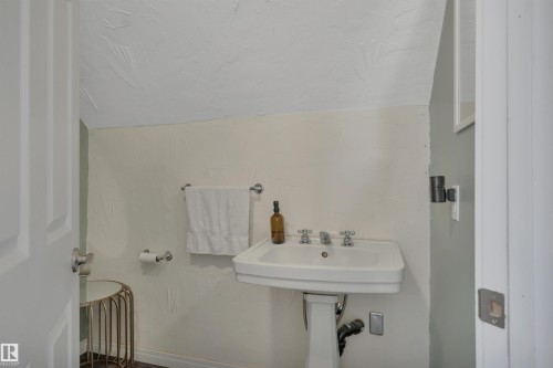 Pedestal sink with chrome fixtures, textured wall finishes, and a sloped ceiling - 305 3 St, Rural Wetaskiwin County, AB - Indoor Photo Showing Bathroom