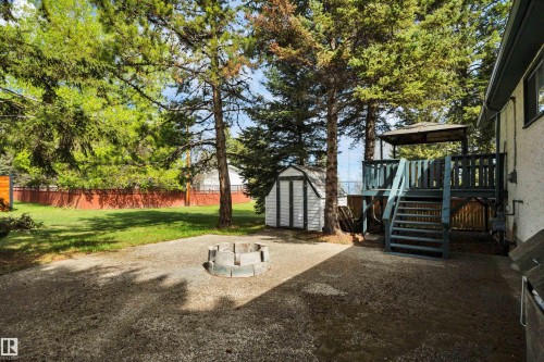 Spacious backyard featuring a multi-level deck with a covered pergola, a concrete patio, a stone fire pit, a storage shed, and mature trees - 305 3 St, Rural Wetaskiwin County, AB - Outdoor