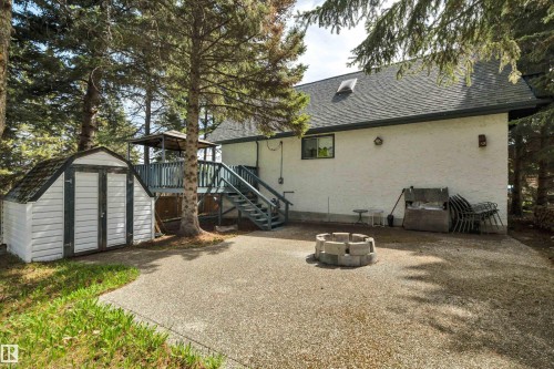 Exposed aggregate patio area featuring a built-in fire pit, a detached storage shed with double doors, and a wood-frame deck with stairs - 305 3 St, Rural Wetaskiwin County, AB - Outdoor