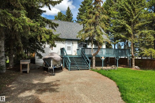 Elevated deck with stairs, white siding, dark gray shingled roof, mature evergreen trees, and a gravel driveway - 305 3 St, Rural Wetaskiwin County, AB - Outdoor With Deck Patio Veranda