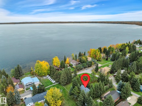 Aerial perspective showcasing a waterfront property with a distinct roofline, surrounded by mature evergreen trees - 305 3 St, Rural Wetaskiwin County, AB - Outdoor With Body Of Water With View