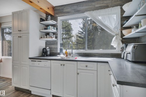 Kitchen featuring white cabinetry, dark countertops, built-in dishwasher, wood-finish flooring, and a window with outdoor scenery - 305 3 St, Rural Wetaskiwin County, AB - Indoor Photo Showing Kitchen