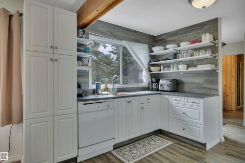 Kitchen featuring white cabinetry, dark countertops, wood-finish flooring, a stainless steel sink, and open shelving - 305 3 St, Rural Wetaskiwin County, AB - Indoor Photo Showing Kitchen