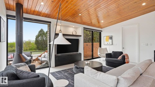 Living area featuring a freestanding fireplace, wood-plank ceiling, recessed lighting, and large glass doors opening to an exterior deck - 6412 Ada Boulevard, Edmonton, AB - Indoor Photo Showing Living Room With Fireplace