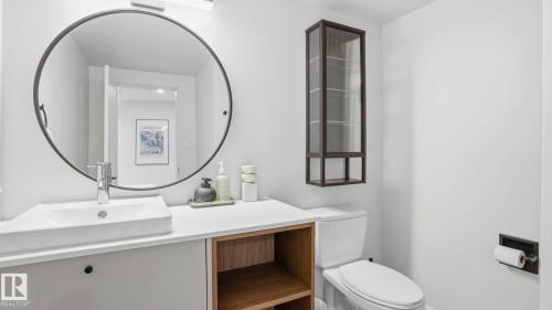 Modern bathroom vanity featuring a rectangular vessel sink with chrome faucet, a large round mirror, and a wood-finish open shelf - 6412 Ada Boulevard, Edmonton, AB - Indoor Photo Showing Bathroom