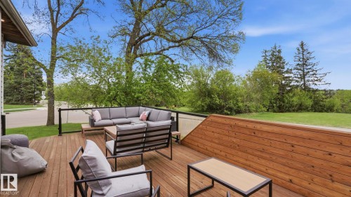 Spacious wood-finish deck with a glass-paneled railing system and a wood-slat privacy wall, surrounded by mature trees - 6412 Ada Boulevard, Edmonton, AB - Outdoor With Deck Patio Veranda