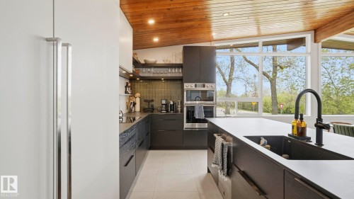 Modern kitchen featuring dark wood-finish cabinetry, white countertops, integrated appliances, and a wood-paneled vaulted ceiling - 6412 Ada Boulevard, Edmonton, AB - Indoor Photo Showing Kitchen With Upgraded Kitchen