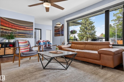 Spacious living area featuring large picture windows, wood-finish flooring, a ceiling fan with integrated lighting, and light blue wall tones - 6707 92B Avenue, Edmonton, AB - Indoor Photo Showing Living Room