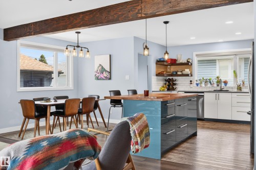 Open-concept living area featuring a large wood beam, wood-finish flooring, and white window trim - 6707 92B Avenue, Edmonton, AB - Indoor