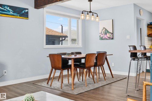 Dining area with wood-finish flooring, a white-framed window, and a dark metal chandelier featuring four clear glass shades - 6707 92B Avenue, Edmonton, AB - Indoor Photo Showing Dining Room