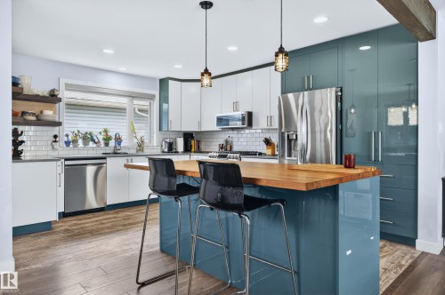Modern kitchen featuring a large island with a wood-finish countertop, stainless steel appliances, white subway tile backsplash, white upper cabinetry, and contrasting blue-green lower cabinetry - 6707 92B Avenue, Edmonton, AB - Indoor Photo Showing Kitchen With Upgraded Kitchen
