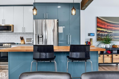 Contemporary kitchen featuring a substantial wood-finish island countertop, stainless steel appliances, white subway tile backsplash, and two-tone cabinetry with blue and white finishes - 6707 92B Avenue, Edmonton, AB - Indoor Photo Showing Kitchen With Upgraded Kitchen