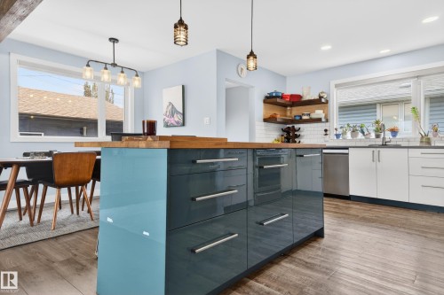 Open-concept kitchen featuring an oversized island with a wood-finish countertop, high-gloss cabinetry, stainless steel appliances, and wood-finish flooring - 6707 92B Avenue, Edmonton, AB - Indoor Photo Showing Kitchen With Upgraded Kitchen