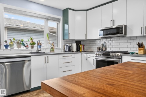 Modern kitchen featuring white cabinetry, stainless steel appliances, grey countertops, white subway tile backsplash, and a wood-finish island countertop - 6707 92B Avenue, Edmonton, AB - Indoor Photo Showing Kitchen With Upgraded Kitchen