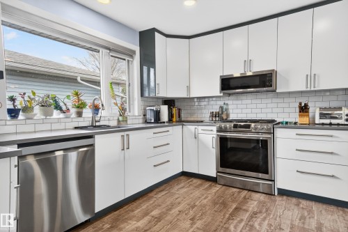 Kitchen featuring white cabinetry with brushed nickel hardware, a stainless steel appliance suite, wood-finish flooring, subway tile backsplash, and a large window above the sink - 6707 92B Avenue, Edmonton, AB - Indoor Photo Showing Kitchen With Upgraded Kitchen