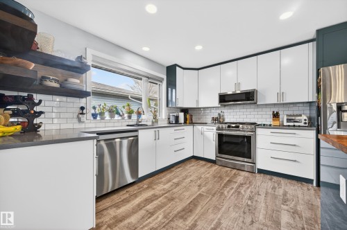 Contemporary kitchen featuring white cabinetry, stainless steel appliances, dark countertops, a subway tile backsplash, and wood-finish flooring - 6707 92B Avenue, Edmonton, AB - Indoor Photo Showing Kitchen With Upgraded Kitchen