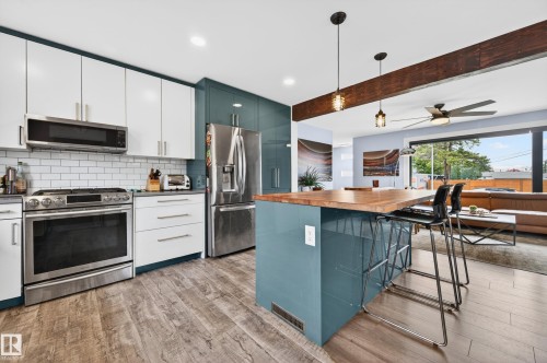 Modern kitchen featuring a central island with a wood countertop, stainless steel appliances, white subway tile backsplash, and wood-finish flooring - 6707 92B Avenue, Edmonton, AB - Indoor Photo Showing Kitchen With Upgraded Kitchen