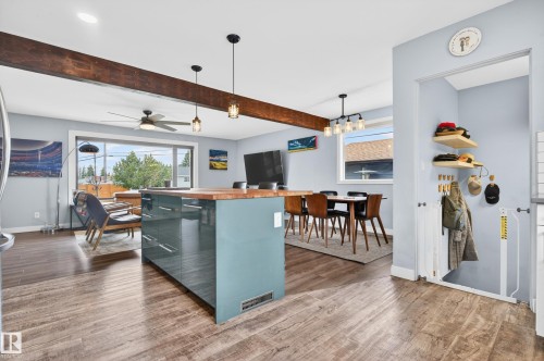 Open-concept living space with wood-finish flooring, a prominent exposed wood beam, and a large central island featuring a light blue-green finish and a wood countertop - 6707 92B Avenue, Edmonton, AB - Indoor