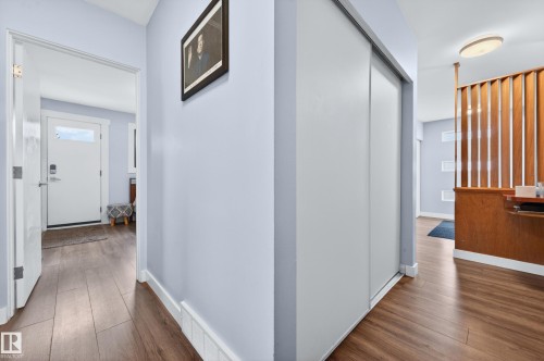 Entryway featuring wood-finish flooring, light blue wall paint, a solid white front door with a transom window, and a built-in closet with sliding white doors - 6707 92B Avenue, Edmonton, AB - Indoor Photo Showing Other Room