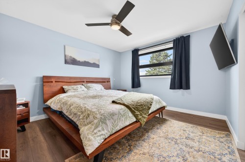 Bedroom featuring wood-finish flooring, light blue walls, and a window with dark curtains - 6707 92B Avenue, Edmonton, AB - Indoor Photo Showing Bedroom