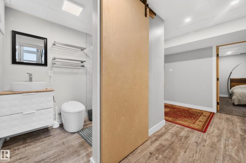 Modern wood-finish flooring extends through this area, featuring a light wood barn door, recessed lighting, and white baseboards - 6707 92B Avenue, Edmonton, AB - Indoor Photo Showing Bathroom