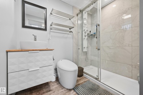 Modern bathroom featuring a glass-enclosed shower with body jets, a vessel sink on a wood-finish countertop vanity, and wood-finish flooring - 6707 92B Avenue, Edmonton, AB - Indoor Photo Showing Bathroom