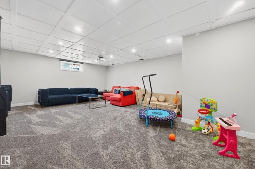 Spacious finished room featuring textured gray carpet, light gray walls, a white coffered ceiling with recessed lighting, and a window providing natural light - 6707 92B Avenue, Edmonton, AB - Indoor