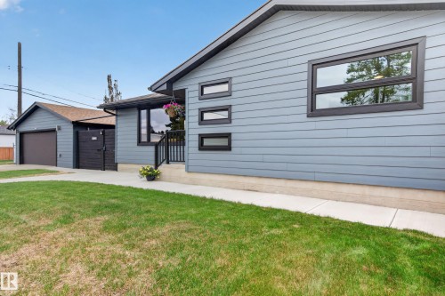 Contemporary exterior featuring light blue siding, black-framed windows, and a detached garage with a brown door - 6707 92B Avenue, Edmonton, AB - Outdoor