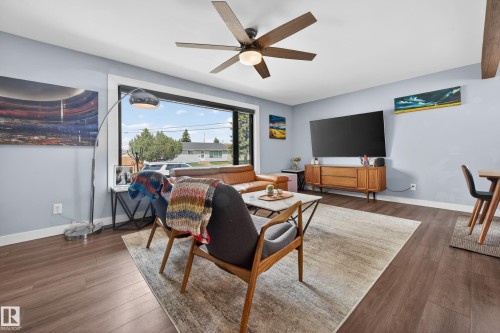 Living area featuring wood-finish flooring, a large picture window, and a ceiling fan with integrated lighting - 6707 92B Avenue, Edmonton, AB - Indoor