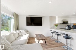 Open-concept living space featuring wood-finish flooring, recessed lighting, expansive windows with drapery, and a peninsula kitchen counter - 