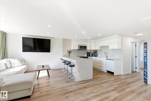 Modern kitchen featuring white cabinetry, integrated appliances, a waterfall island with seating, and wood-finish flooring - 108 10105 95 Street, Edmonton, AB - Indoor
