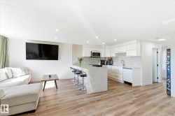 Modern kitchen featuring white cabinetry, integrated appliances, a waterfall island with seating, and wood-finish flooring - 