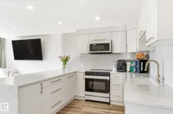 Modern kitchen featuring white cabinetry with gold-tone hardware, a matching white-finish range and microwave, light-toned countertops, and wood-finish flooring - 