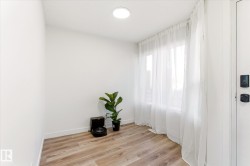 Room featuring bright white walls, contemporary wood-finish flooring, and a large window with sheer white drapery - 