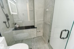 Contemporary shower enclosure featuring full-height glass panels, matte black shower fixtures, a built-in bench with a dark countertop, and large format gray tile surrounds - 