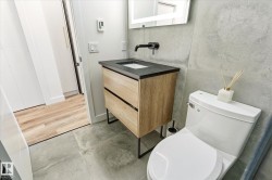 Modern bathroom featuring a wood-finish vanity with a black countertop, a wall-mounted matte black faucet, and a large illuminated mirror - 