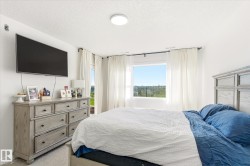 Spacious bedroom featuring multiple windows, a wall-mounted television, and light-colored carpeting - 
