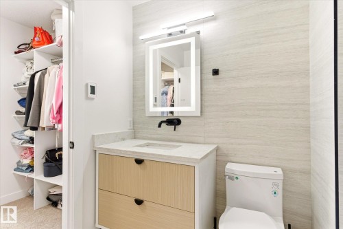 Modern vanity featuring two-tone cabinetry, a light-toned countertop, and an illuminated mirror - 108 10105 95 Street, Edmonton, AB - Indoor Photo Showing Bathroom