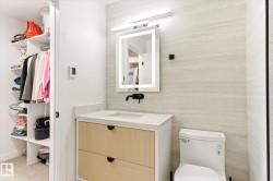 Modern vanity featuring two-tone cabinetry, a light-toned countertop, and an illuminated mirror - 