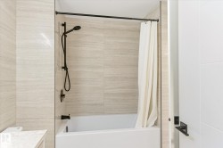 Bathtub and shower combination featuring floor-to-ceiling textured tile surround, matte black shower fixtures including a handheld showerhead, and a white soaking tub - 