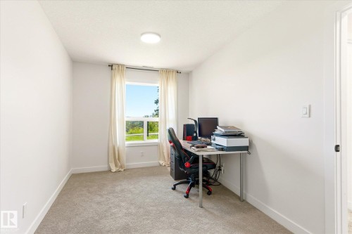 Room featuring a window with exterior scenery, light-colored carpeting, white walls, a ceiling-mounted light fixture, and white baseboards - 108 10105 95 Street, Edmonton, AB - Indoor Photo Showing Office