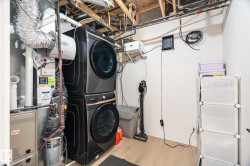 Utility room featuring a stacked washer and dryer, exposed ceiling joists, and a forced air furnace - 